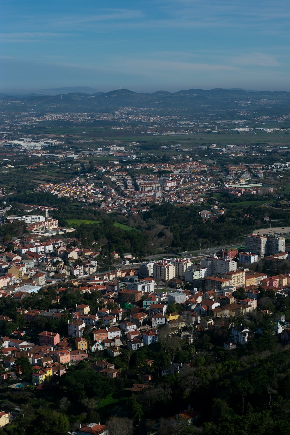 A sprawling town with red-tiled roofs nestled among rolling green hills.