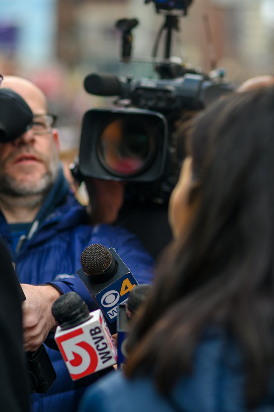 Journalists with microphones interview someone off-camera.
