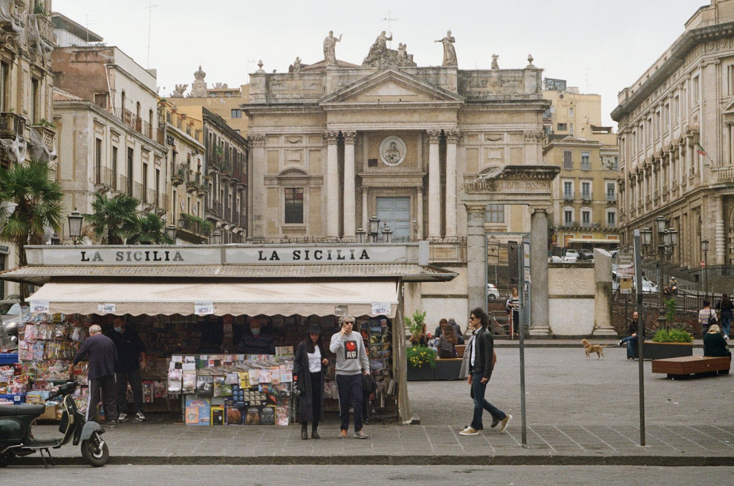 People walk and gather in a busy city square.